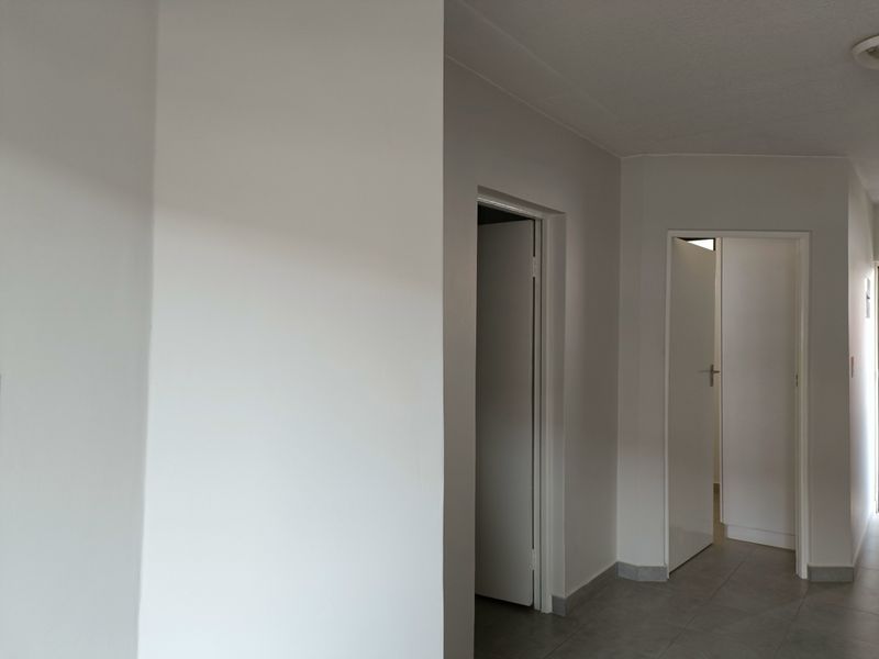 A clean, neutral hallway featuring tiled flooring and multiple internal doorways providing access to adjacent rooms.