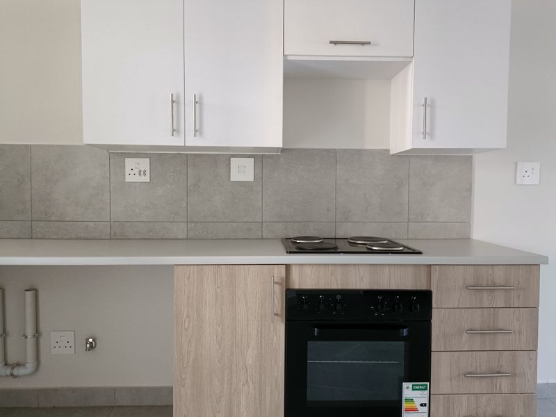 Modern kitchen featuring light wood-finish cabinetry, stone-look tiled backsplash, built-in oven, electric hob, and dedicated plumbing connections for appliances.
