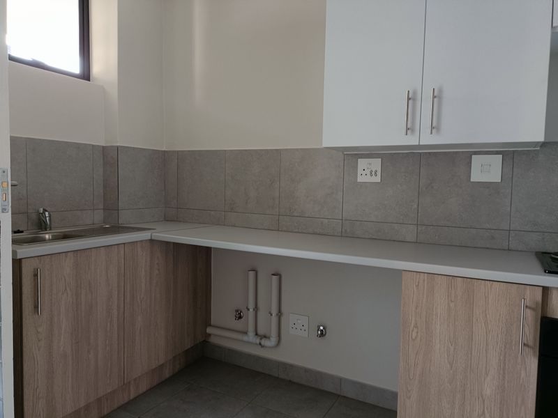 A clean, modern kitchen area featuring light wood-finish cabinetry, grey tiled backsplash, and dedicated plumbing connections for appliances.