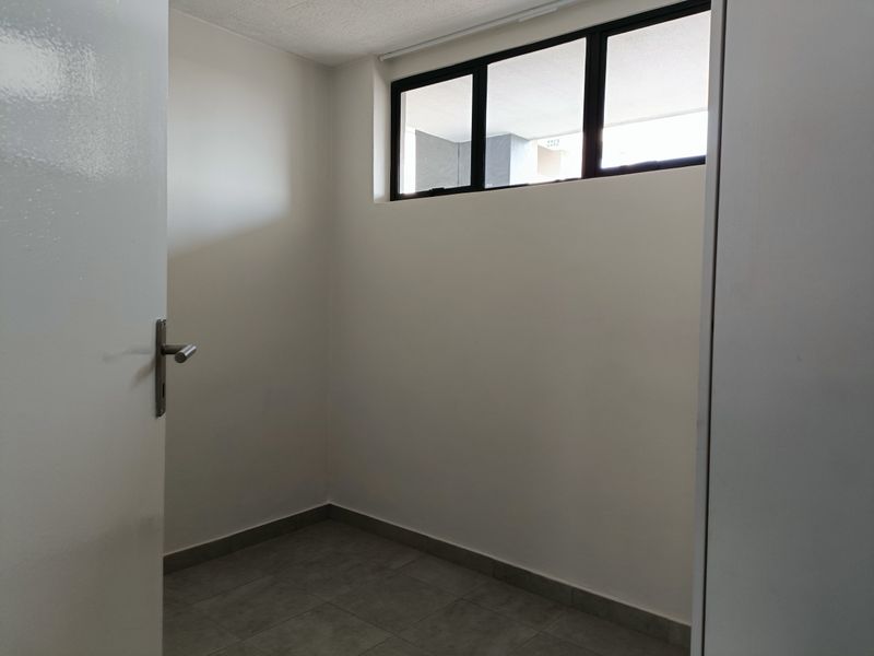 A clean, empty entrance area featuring neutral tiled flooring and a black-framed window, providing a bright and versatile space.