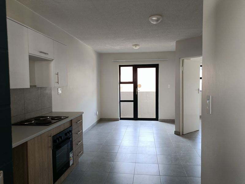 An open-plan kitchen and living area featuring modern cabinetry, an electric hob, oven, and tiled flooring, leading to an outdoor balcony area.