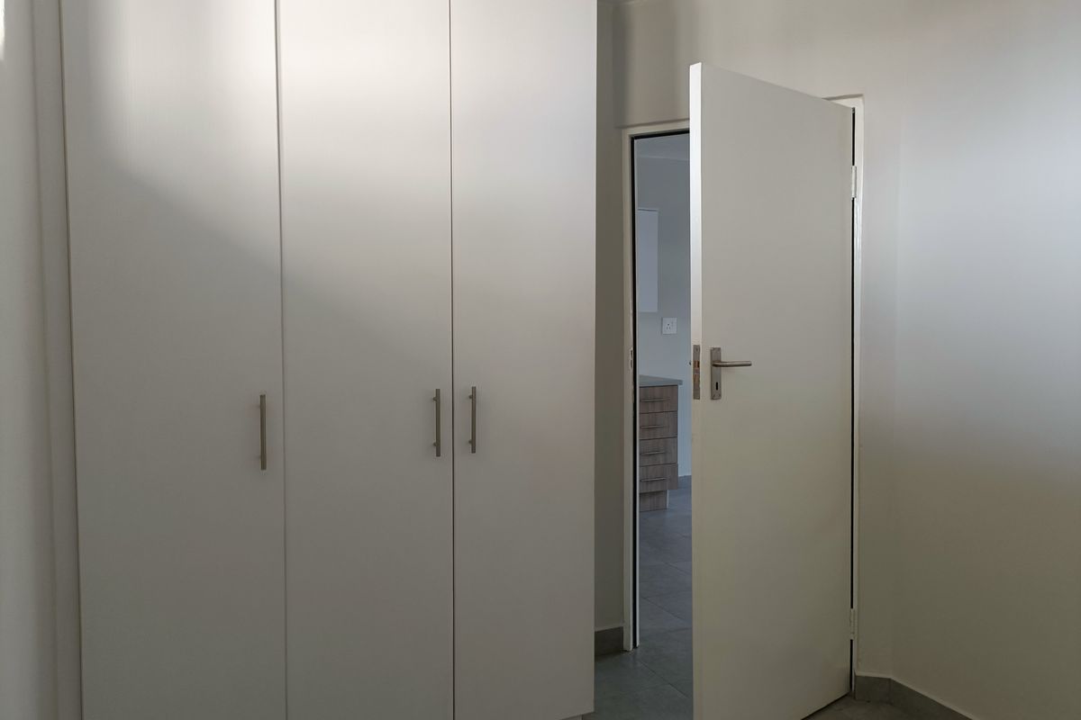 A clean, minimalist bedroom featuring white built-in cupboards and neutral tiled flooring, offering a bright and functional space.