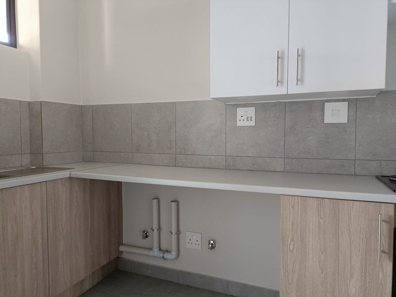 Modern kitchen area featuring light wood-look cabinetry, stone-style tiled backsplash, and dedicated plumbing connections for a washing machine or dishwasher.