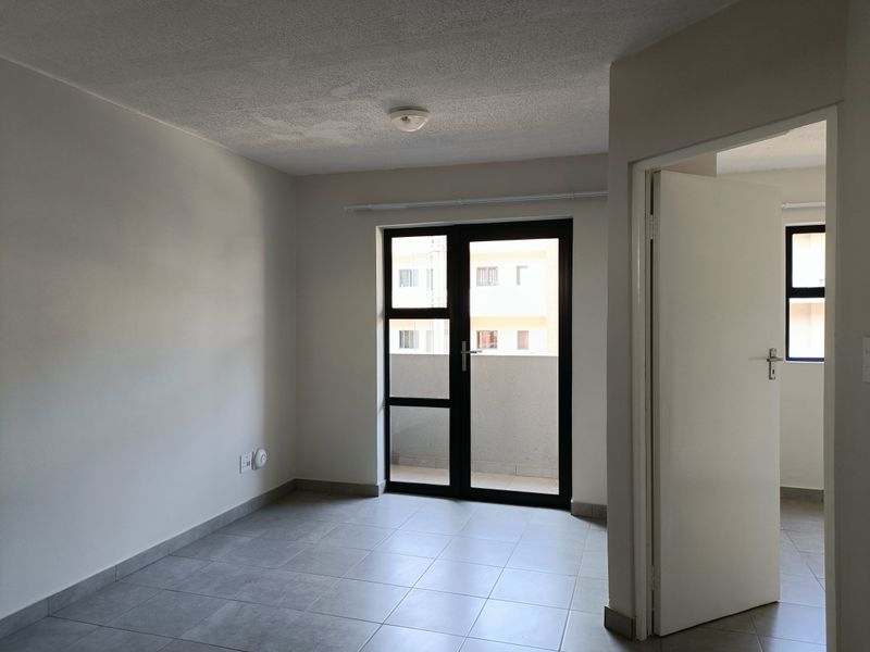 An empty, neutrally painted living area featuring tiled flooring and a glass door providing access to a balcony.