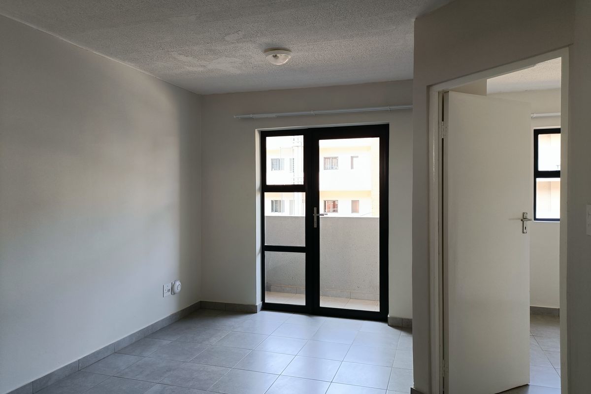 An empty, neutrally painted living area featuring tiled flooring and a glass door providing access to a balcony.