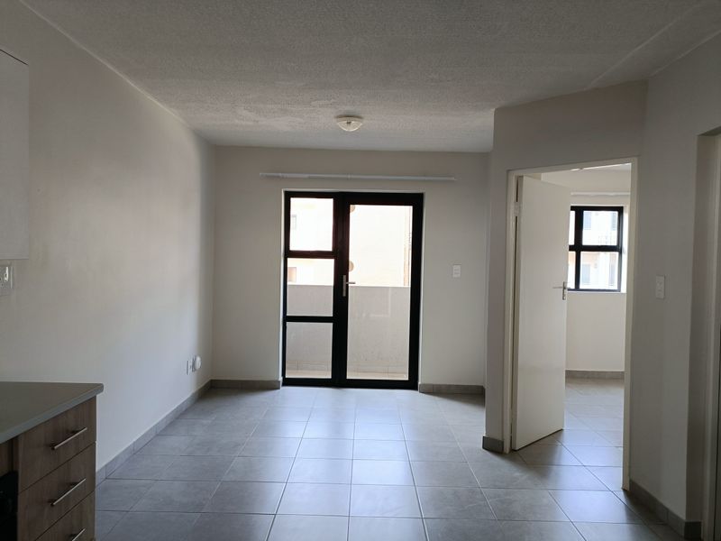 An open-plan living area featuring neutral tiled flooring, modern glass panel doors leading to a balcony, and clean, minimalist finishes.