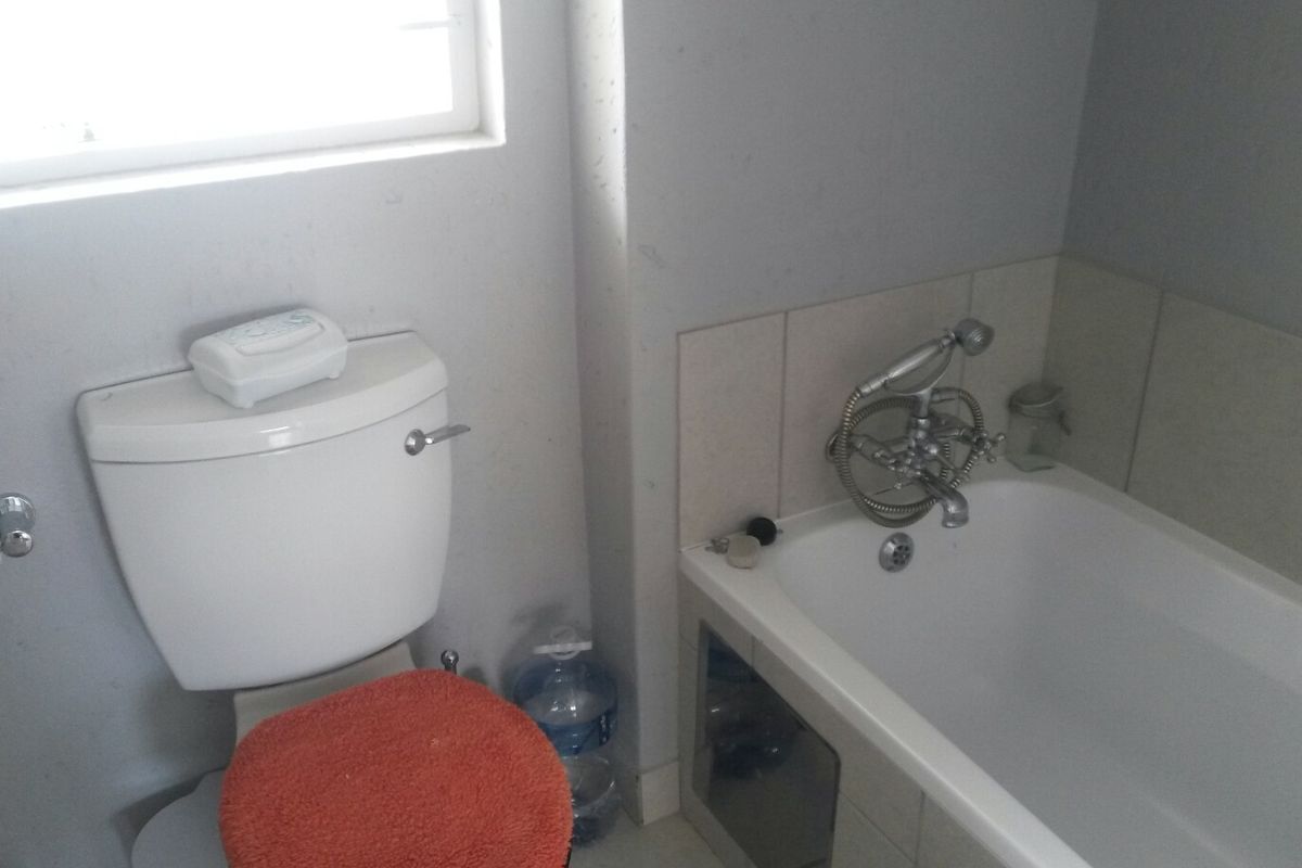 A compact bathroom featuring a standard bathtub with a shower mixer and a toilet, requiring cosmetic updates to the wall finishes.