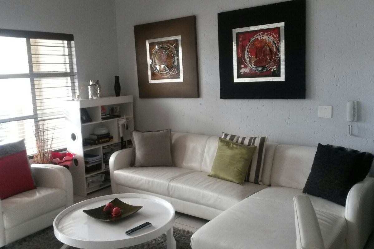 A comfortable living room featuring an intercom system, aluminium window frames, and fitted venetian blinds, providing a functional and well-lit space.