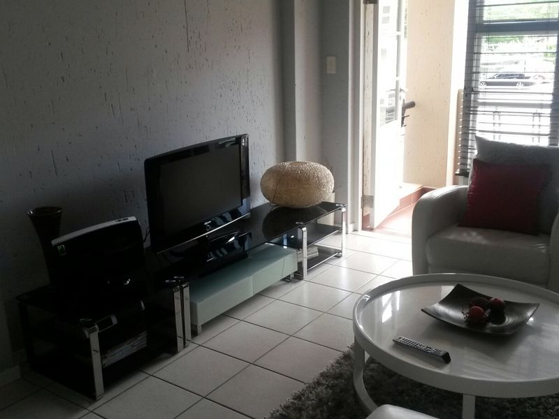 A living room area featuring tiled flooring, a sliding door leading to an outdoor space, and venetian blinds.