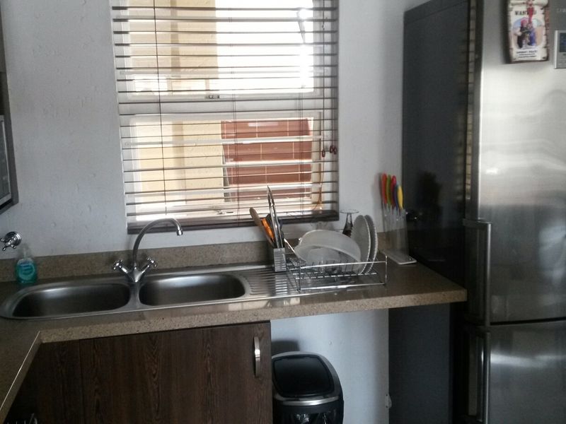 A functional kitchen area featuring a double bowl stainless steel sink, laminate countertops, and built-in cabinetry with a window providing natural light.