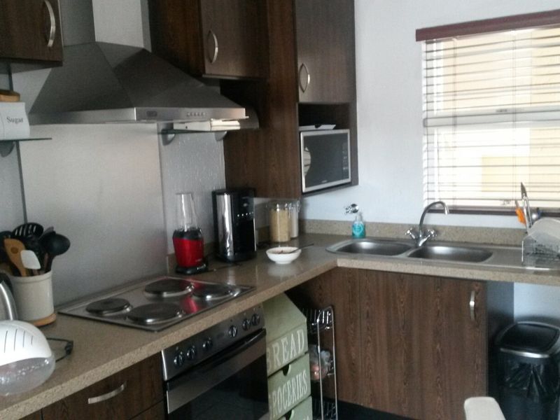 A functional kitchen featuring dark wood cabinetry, laminate countertops, a built-in oven with electric hob, and a stainless steel extractor fan.