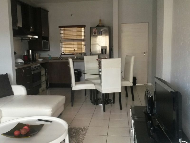 Open-plan living and kitchen area featuring tiled flooring, dark wood cabinetry, and integrated kitchen appliances in a functional apartment layout.