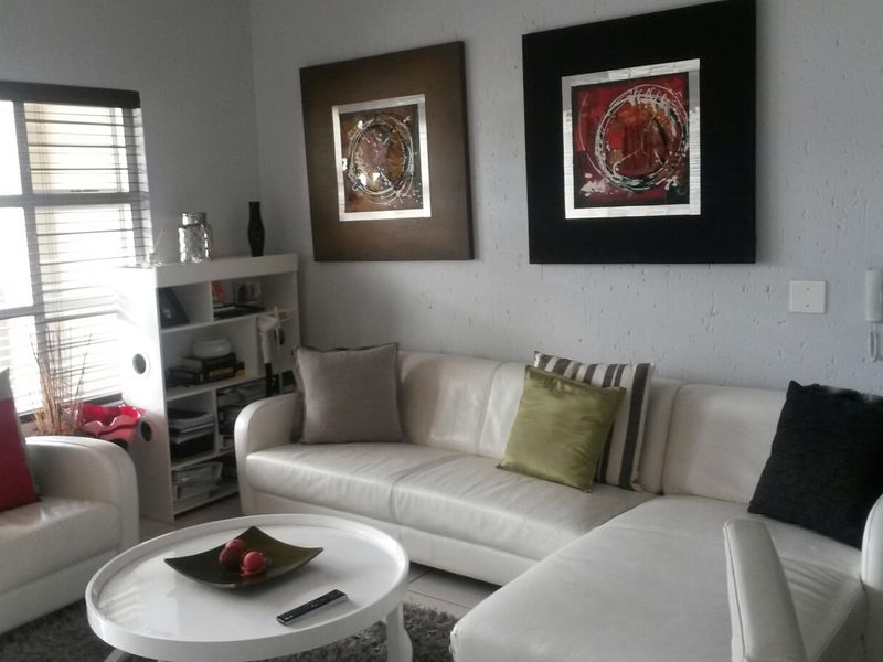 A comfortable living room featuring an intercom system, aluminium window frames, and fitted venetian blinds, providing a functional and well-lit space.