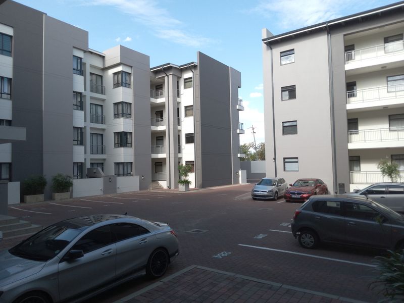 View of the paved parking courtyard between modern multi-story apartment buildings featuring balconies and clean exterior finishes.