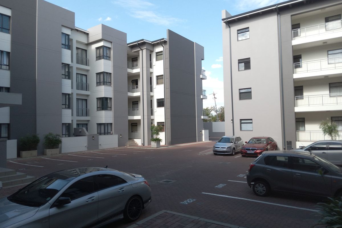 View of the paved parking courtyard between modern multi-story apartment buildings featuring balconies and clean exterior finishes.