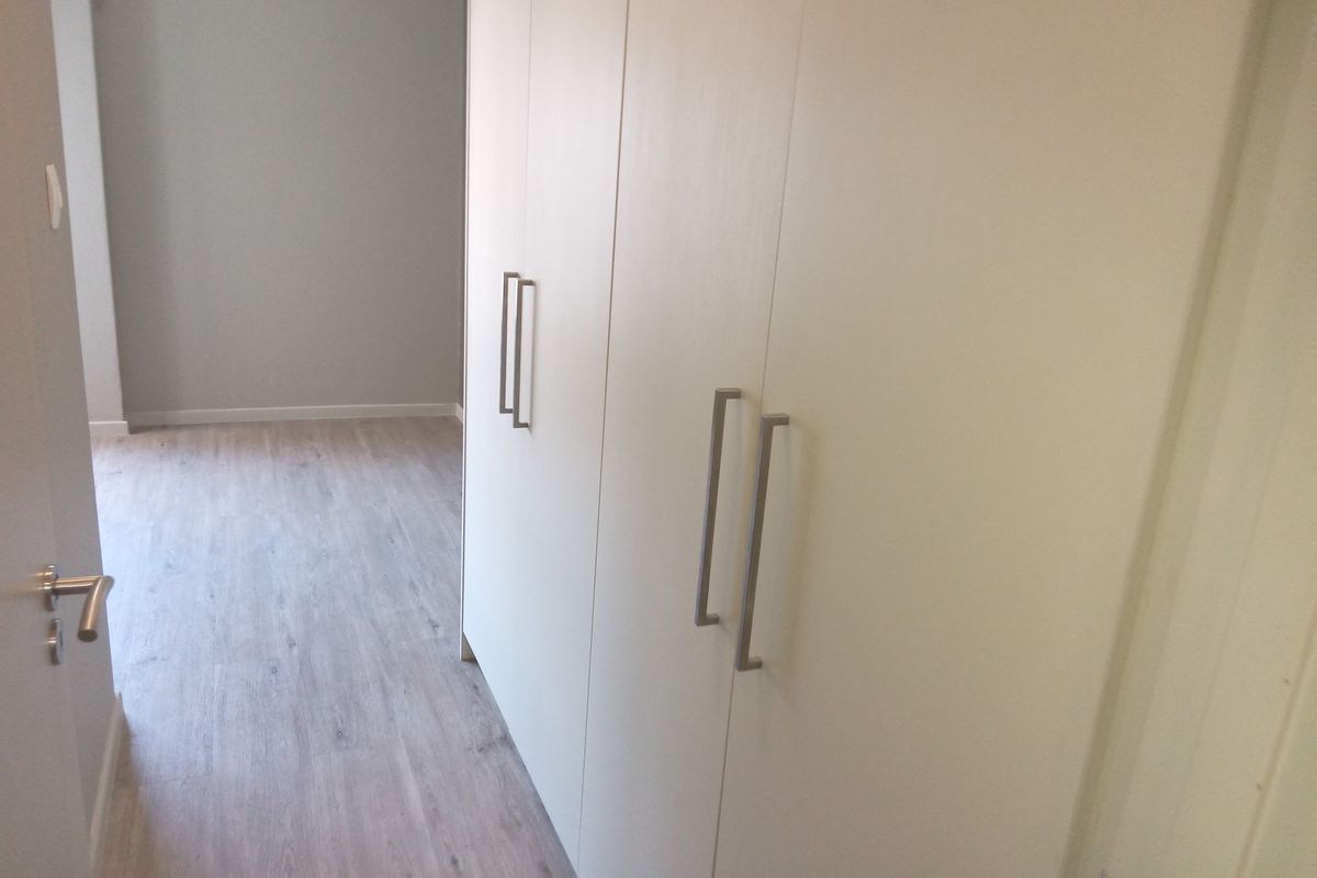 A bright, empty bedroom featuring modern built-in cupboards and light-toned laminate flooring, offering a clean and neutral space ready for personalization.
