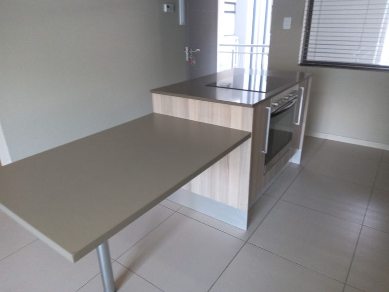 Modern kitchen featuring a central island with an integrated oven and hob, complemented by neutral tiled flooring and clean cabinetry finishes.