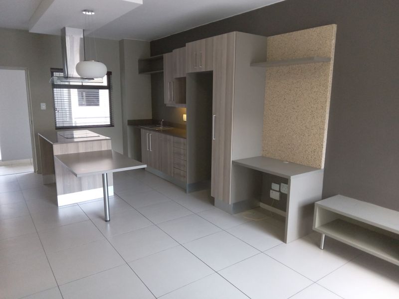 Modern open-plan kitchen and living area featuring sleek built-in cabinetry, a functional kitchen island with extractor fan, and a dedicated built-in desk space.