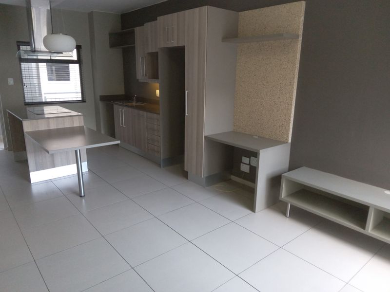 Modern open-plan living area featuring a sleek kitchen with built-in cabinetry, an island, and a dedicated workspace, finished with neutral floor tiles.