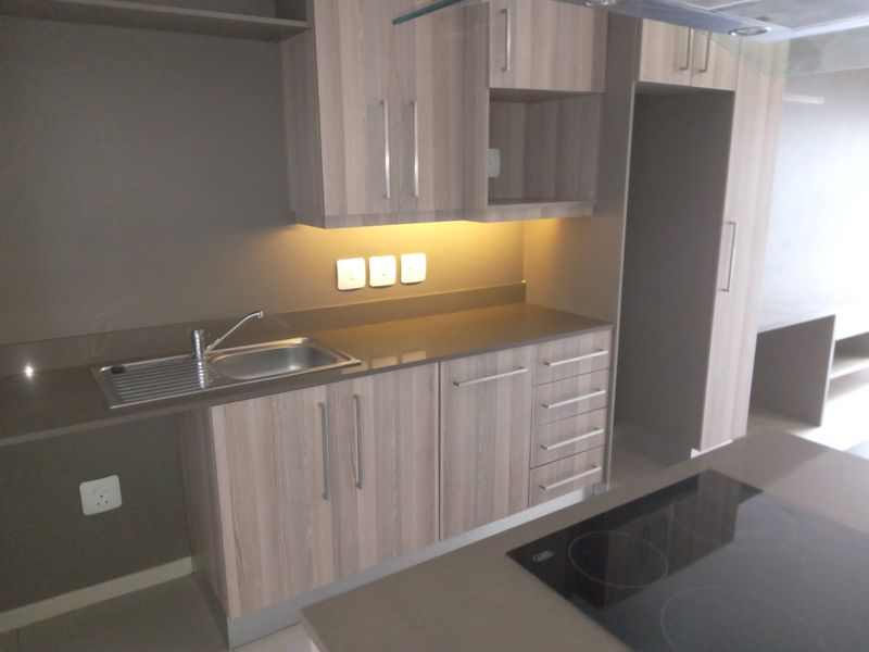Modern kitchen featuring light wood-grain cabinetry, stone countertops, integrated hob, and under-cabinet lighting in a clean, functional layout.