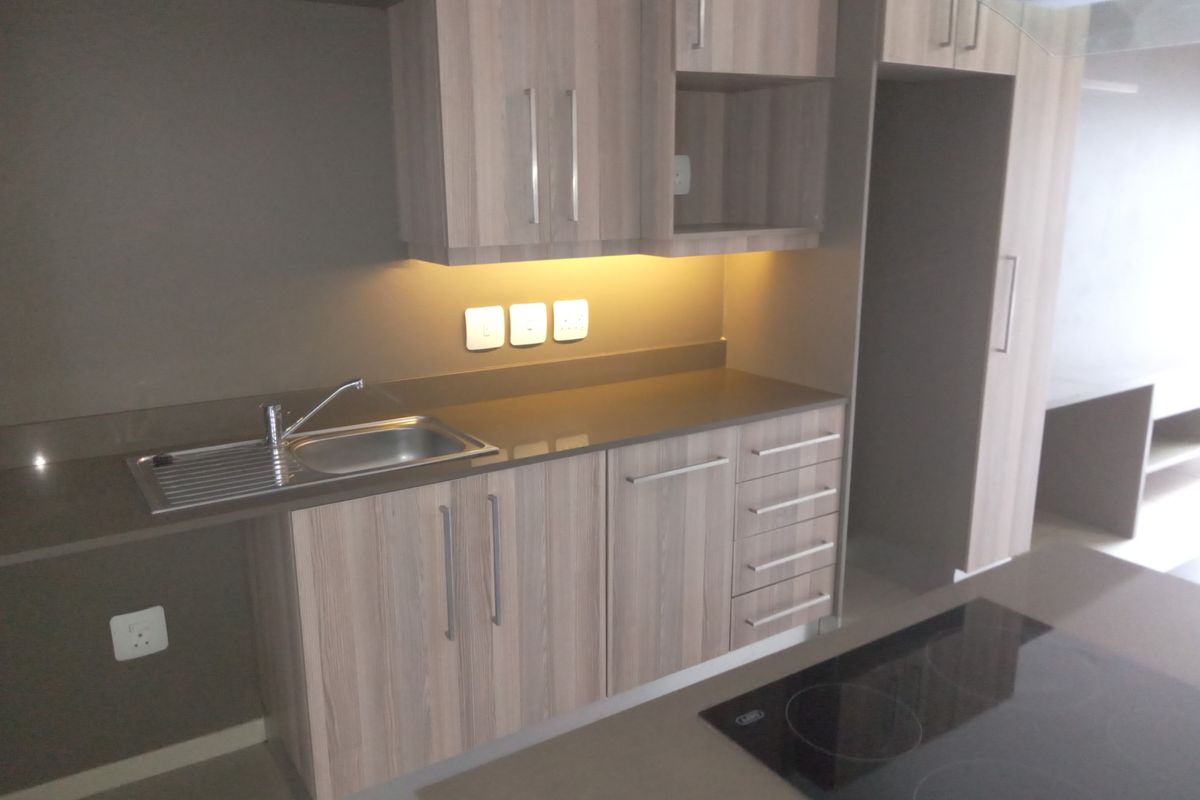 Modern kitchen featuring light wood-grain cabinetry, stone countertops, integrated hob, and under-cabinet lighting in a clean, functional layout.