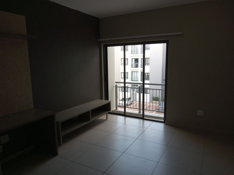 An empty living room featuring tiled flooring and a sliding glass door that opens onto a small balcony.