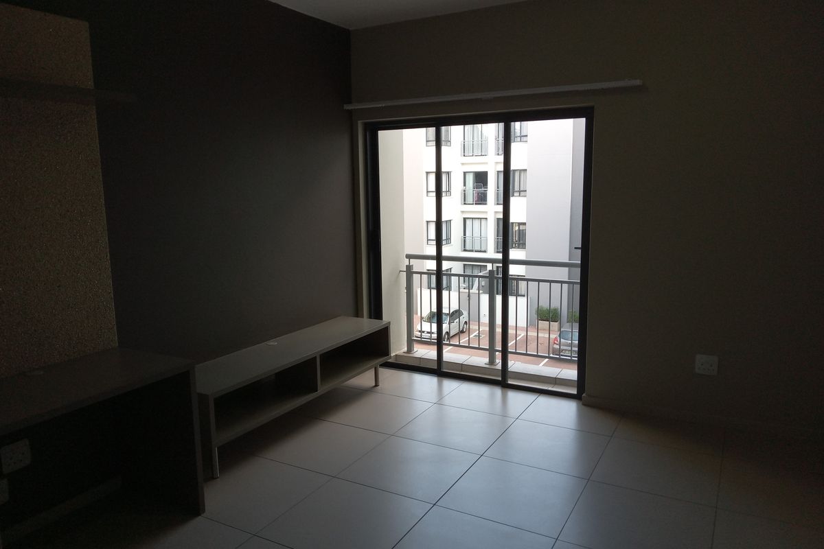 An empty living room featuring tiled flooring and a sliding glass door that opens onto a small balcony.