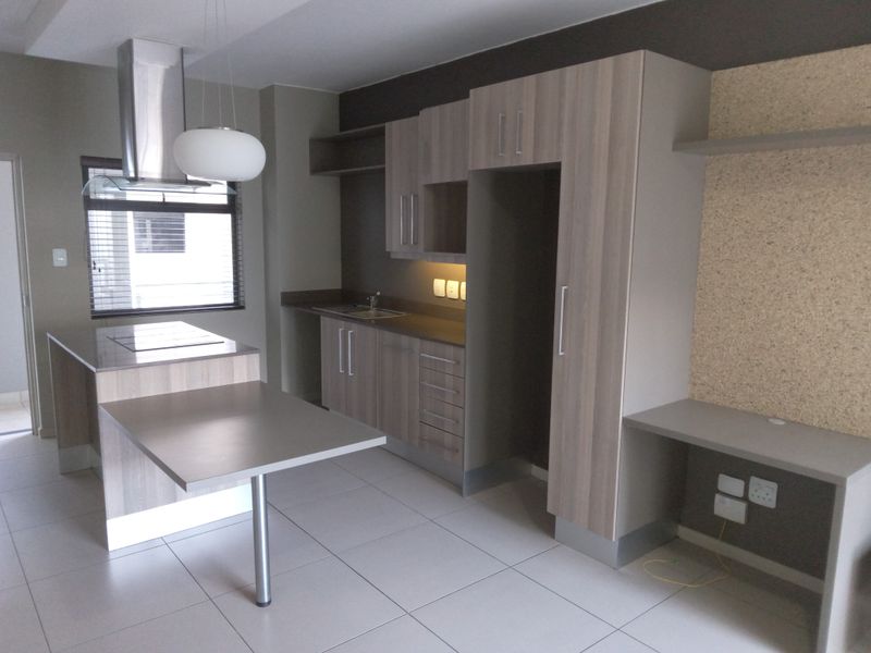 Modern kitchen featuring light wood-tone cabinetry, a central island with integrated hob, stainless steel extractor fan, and a dedicated built-in workspace area.