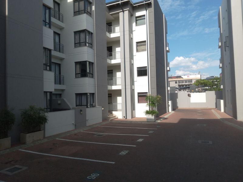 Exterior view of a modern apartment complex featuring paved parking bays and multi-story residential units with balconies.