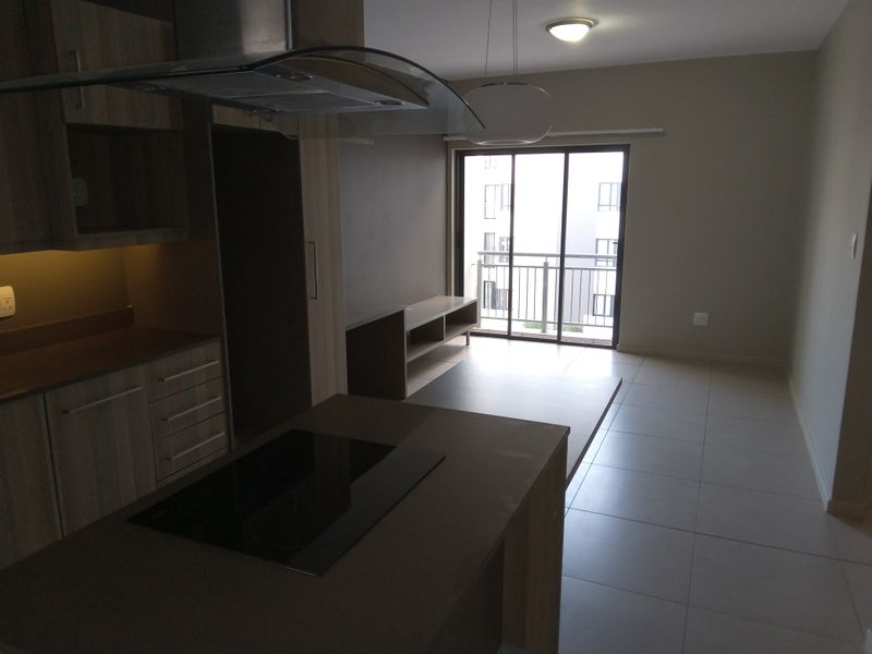 Modern open-plan kitchen and living area featuring sleek cabinetry, a built-in hob, and direct access to a private balcony through sliding glass doors.