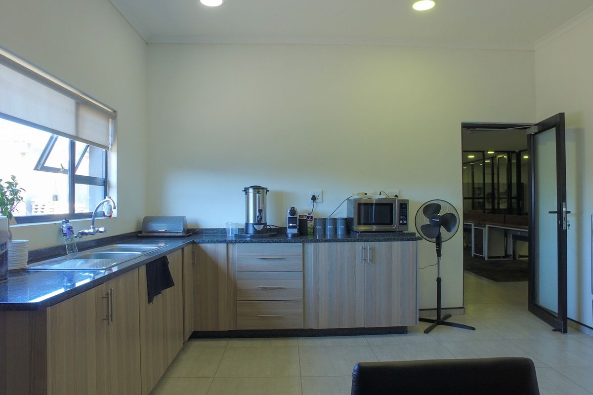 A functional office kitchenette featuring light wood-finish cabinetry, granite countertops, a double sink, and modern recessed lighting.