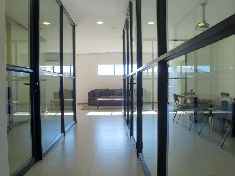 A modern office hallway featuring glass partition walls, tiled flooring, and recessed lighting, providing a clean and professional workspace aesthetic.