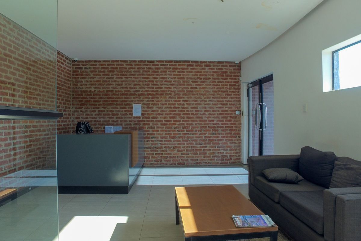Office reception area featuring an exposed brick feature wall, tiled flooring, and a built-in reception desk with glass partition.