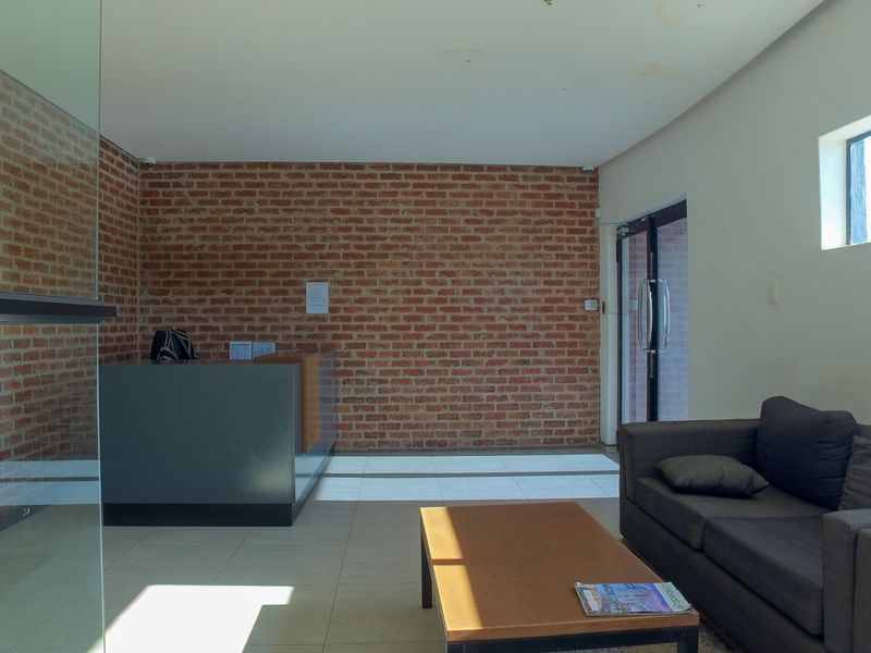 Office reception area featuring an exposed brick feature wall, tiled flooring, and a built-in reception desk with glass partition.