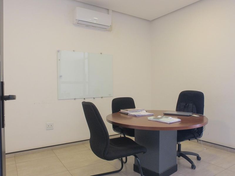 A clean, professional office space featuring tiled flooring, a wall-mounted air conditioning unit, and a glass whiteboard, suitable for meetings or focused work.