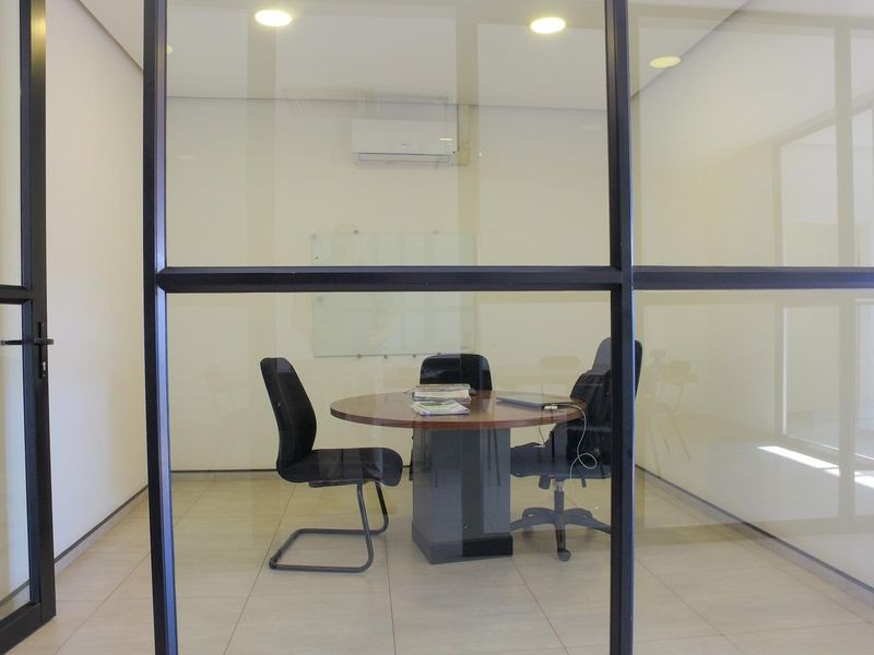 A modern office meeting room featuring a glass partition wall, tiled flooring, recessed lighting, and a wall-mounted air conditioning unit.