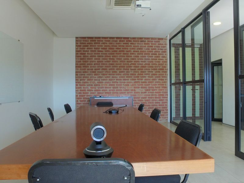 Modern office meeting room featuring an exposed brick wall, glass partitions, and integrated ceiling lighting, providing a professional and bright workspace environment.