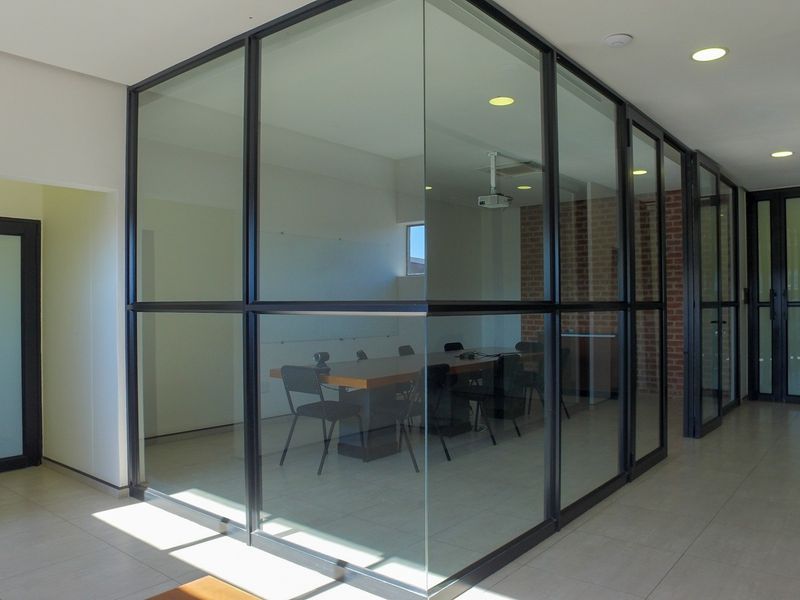 Modern office space featuring a glass-enclosed meeting room, exposed brick accents, and sleek black metal framing, providing a professional and contemporary work environment.