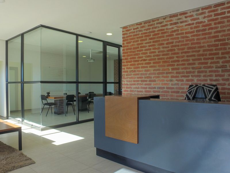 Modern office reception area featuring an exposed brick feature wall, glass-partitioned meeting room, and sleek reception desk with tiled flooring.