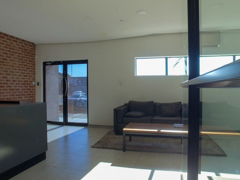Modern office reception area featuring an exposed brick feature wall, tiled flooring, glass partitioning, and a built-in reception desk.