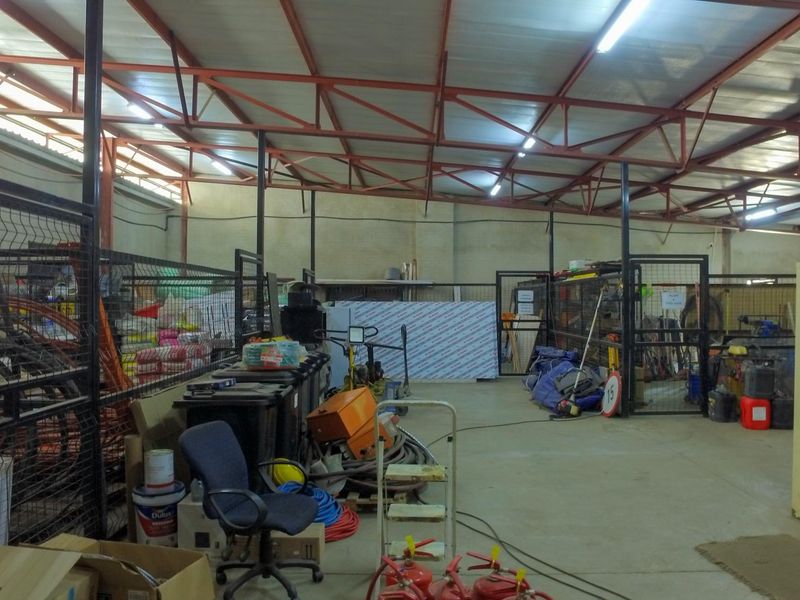 Spacious industrial utility area featuring exposed steel roof trusses, concrete flooring, and metal mesh partitioning for organized storage or workspace operations.