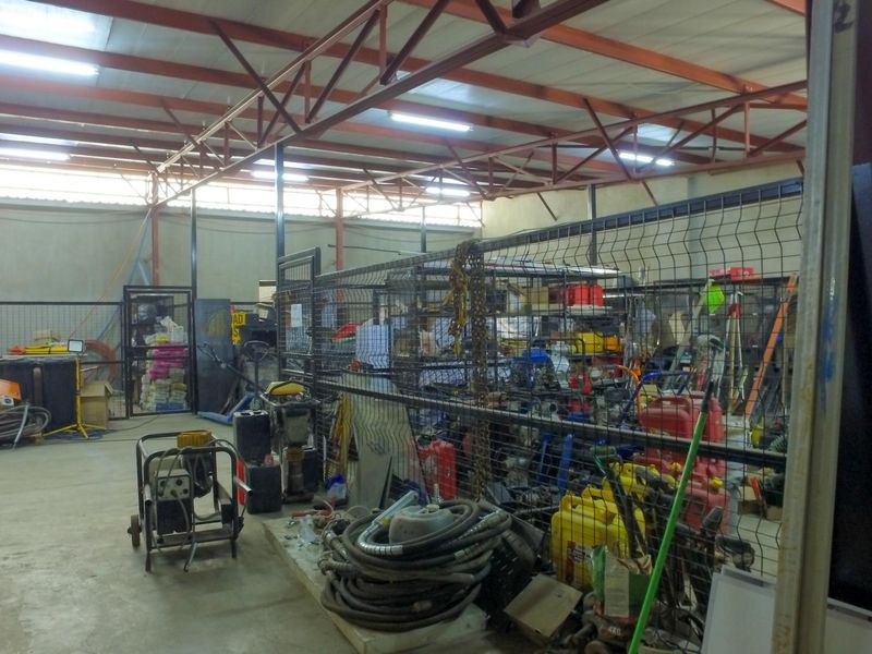 Industrial utility space featuring exposed steel roof trusses, concrete flooring, and wire mesh partitioning for secure storage.