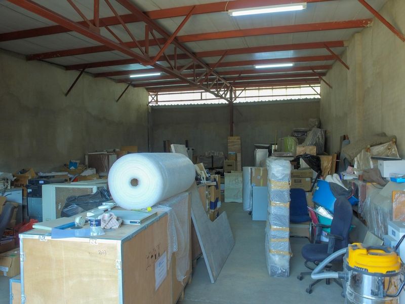 Industrial utility space featuring exposed steel roof trusses, concrete flooring, and unpainted masonry walls, suitable for storage or workshop use.