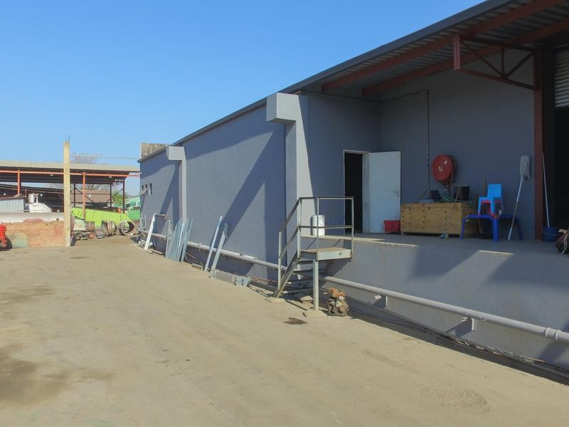 Industrial exterior view showing a loading dock area with a roller shutter door, steel staircase, and concrete yard space.