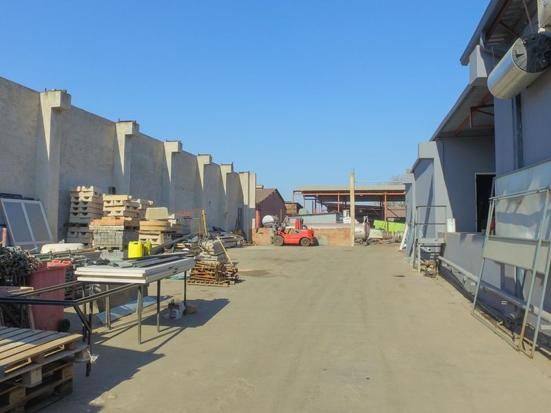An industrial rear yard area featuring a concrete surface, perimeter walling, and access to the side of the main industrial building structure.