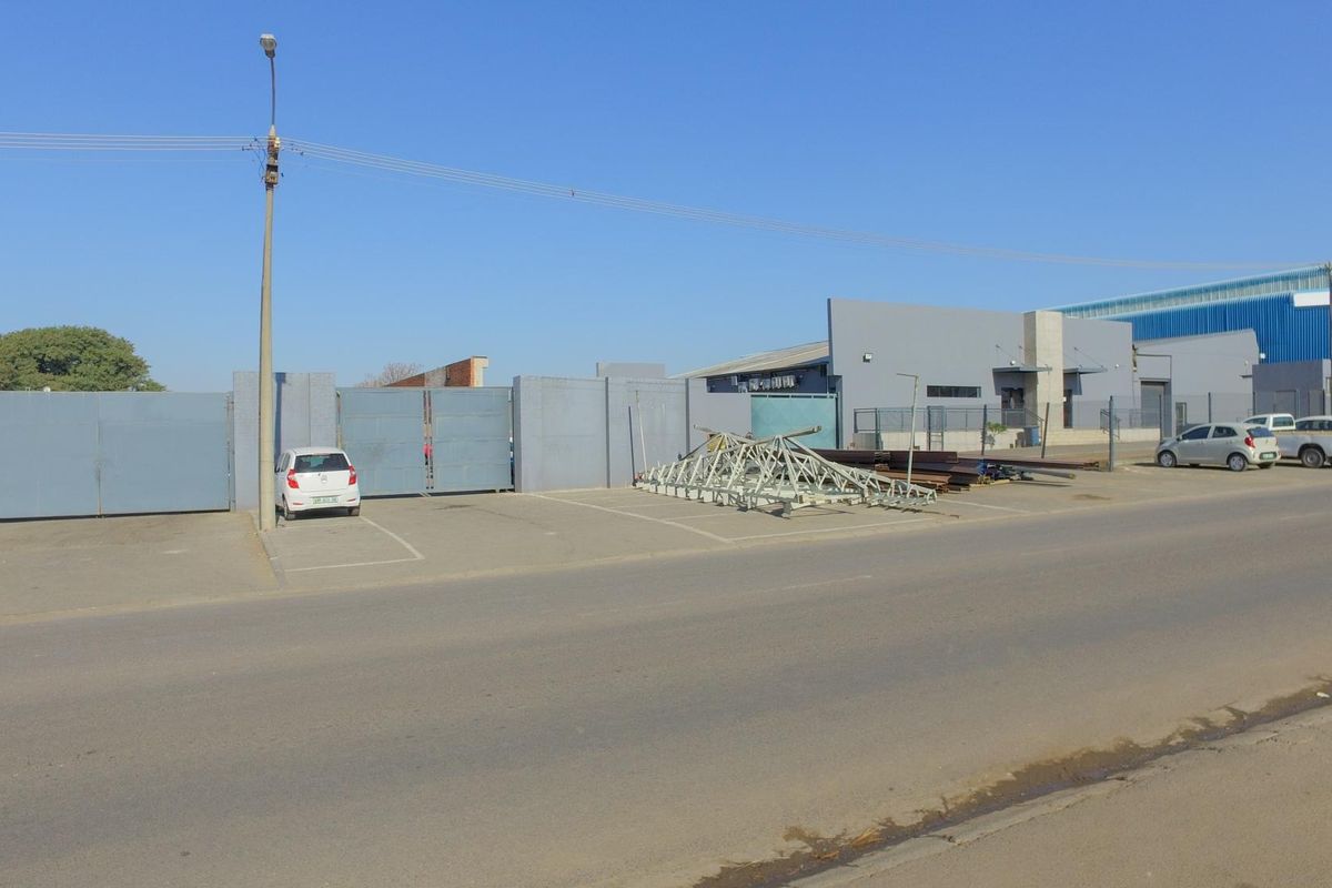 Street-level view of an industrial property featuring a gated perimeter, paved parking area, and a functional warehouse building facade.
