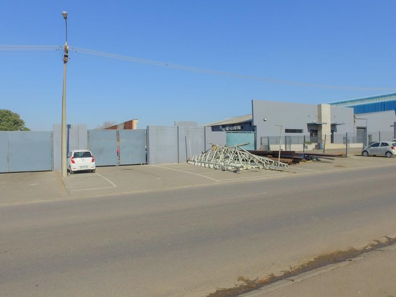 Street-level view of an industrial property featuring a gated perimeter, paved parking area, and a functional warehouse building facade.