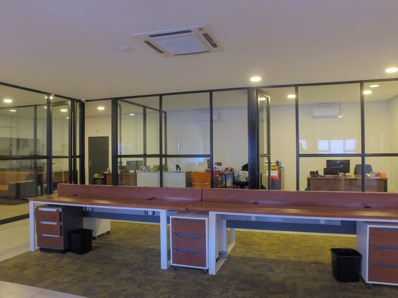 Modern open-plan office space featuring glass partition walls, integrated desk workstations, and recessed ceiling lighting with climate control.