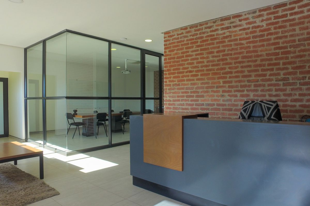 Modern industrial-style office reception area featuring an exposed brick feature wall, sleek glass-partitioned meeting room, and contemporary reception desk.
