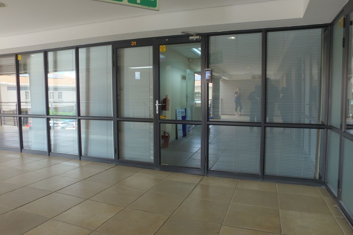 A professional office entrance featuring a modern glass partition wall, aluminum framing, and tiled flooring, providing a clean and accessible workspace entry.
